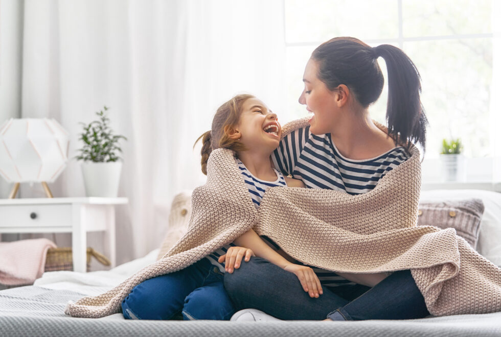Mom and daughter sitting on couch with blanket