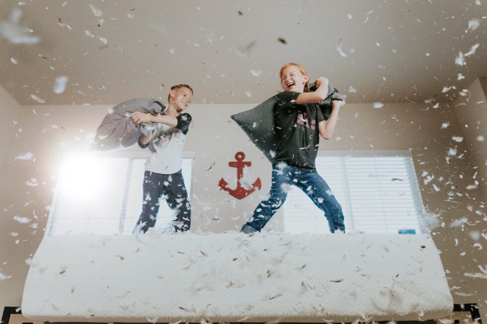 Children jumping on bed having a pillow fight with feathers flying