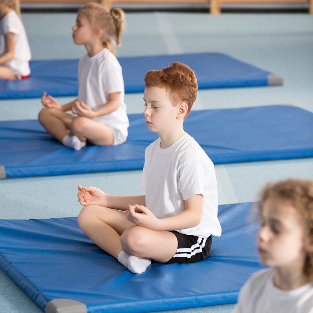 Children sitting on mats meditating wearing white tshirt and shorts