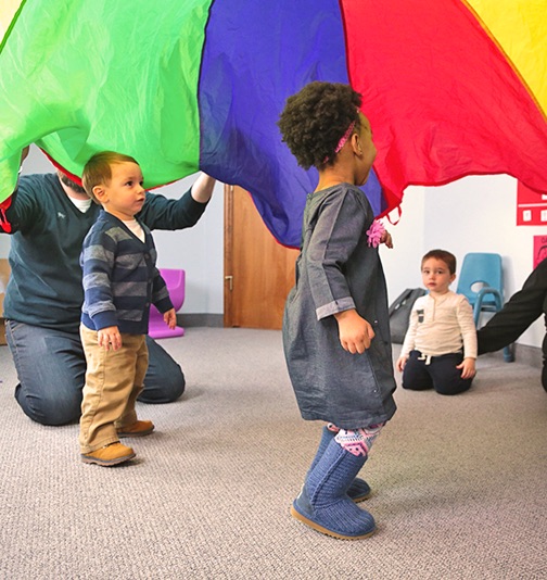 Students playing in classroom with colorful parachute