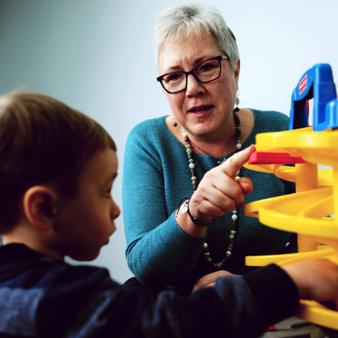 Older woman wearing blue shirt, playing with toys with younger boy