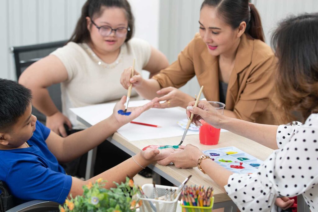 Women painting on hands of child sitting at desk