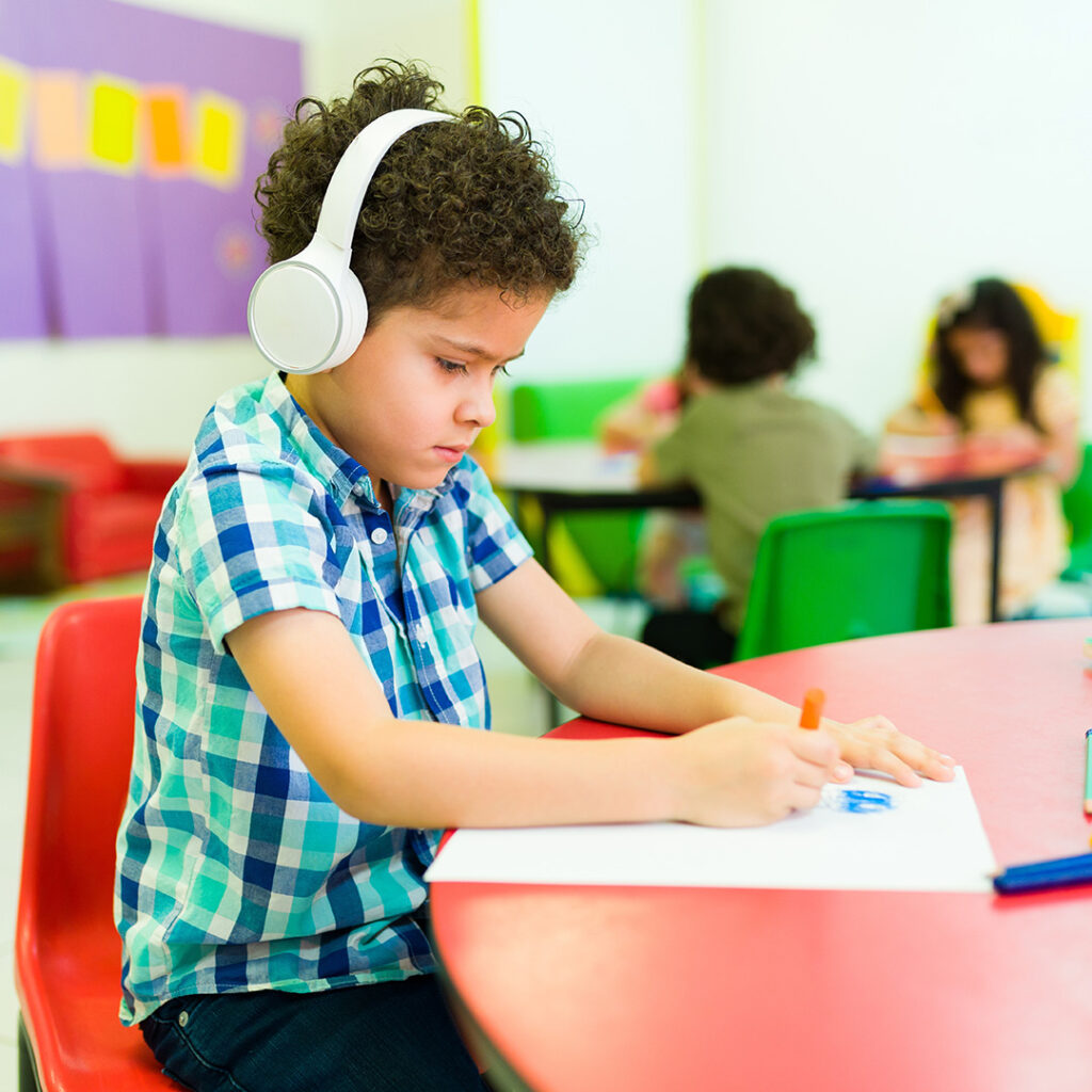 Little boy wearing button down and headphones drawing on paper